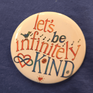 Let's be infinitely Kind button on blue shirt